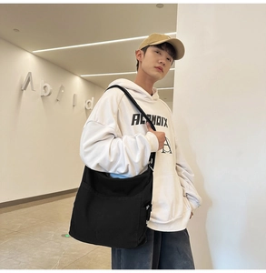 Detailed view of black canvas shoulder bag with wide strap and side pocket