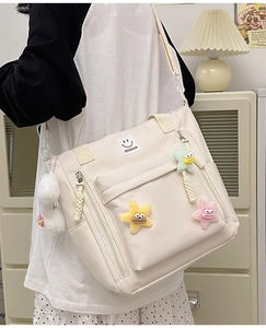 Detail of a beige nylon shoulder bag featuring a smiley patch and cute plush star charms
