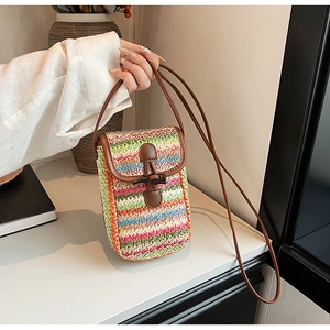 Detail of a small colorful straw woven crossbody bag with brown faux leather strap