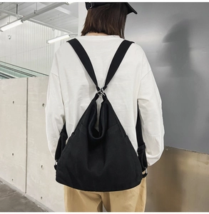 Detail view of black denim backpack featuring unique X-shaped cross hook strap design