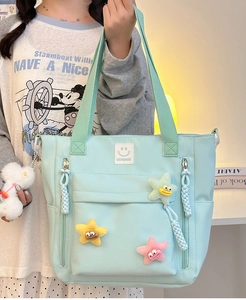 Close-up of light blue nylon tote bag with colorful plush star charms and front pockets