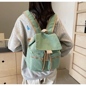 Detalle de una mochila de lona verde claro con cierre de solapa y bolsillos laterales con cremallera