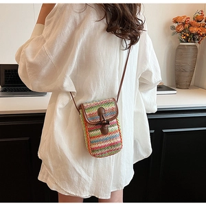 Close-up of rainbow striped straw woven crossbody bag with brown leather strap and horn toggle