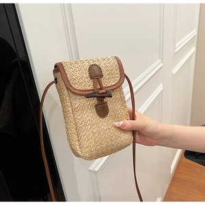 Detail of straw woven crossbody bag featuring brown leather trim and retro horn buckle