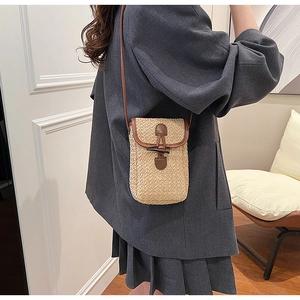 Detailed close-up of straw woven crossbody bag with brown leather trim and toggle closure