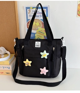 Detail of black nylon tote bag with colorful plush star charms and front logo patch