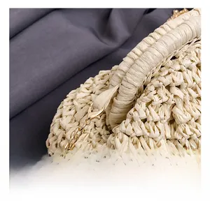 Detail shot of golden metal chain link and lobster clasp on a beige straw crossbody bag