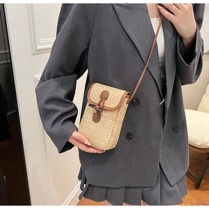 Detail of woven straw crossbody bag with brown leather trim and retro horn toggle buckle