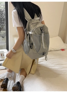 Detail of light grey nylon backpack showing side mesh pocket and utility buckle strap
