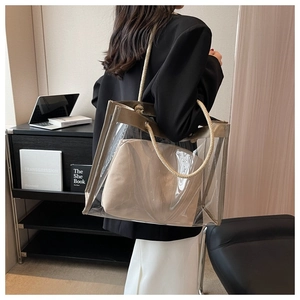 Transparent PVC tote bag with beige inner pouch shown on shoulder in a modern home office