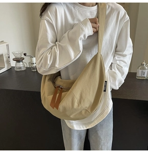 Detail of khaki canvas half-moon crossbody bag with leather zipper and brand tag