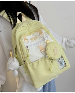 Detail of light yellow nylon backpack showing bear charm and circular pendant attachment