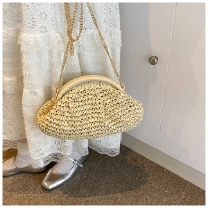Detail of hand-woven straw crossbody bag with gold metal frame and delicate chain strap