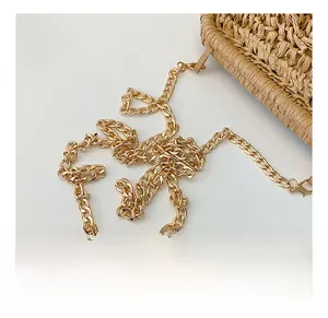 Détail de la bandoulière en chaîne dorée sur un mini sac en paille tissée coquille