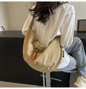 Detail of a large khaki canvas crescent bag showing side brand tag and leather zipper pull