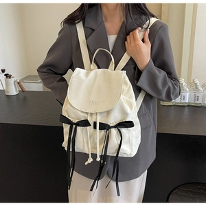 Detail of minimalist beige PU leather backpack with Nika embroidery and black ribbon bows