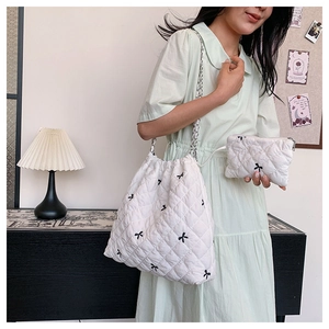 Detail of white quilted nylon shoulder bag set with black bow embroidery and chain strap