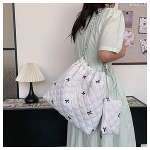 Detail of white quilted tote bag with black bow embroidery and silver chain straps