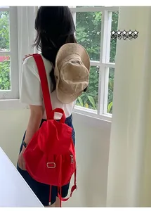 Detail of red nylon drawstring backpack with flap and khaki bucket hat in outdoor setting