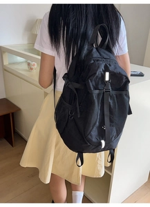 Detail of black nylon backpack featuring reflective straps and mesh side pockets on model