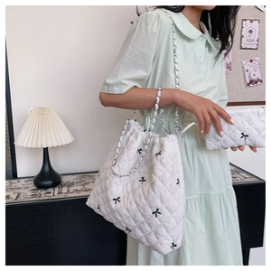 Detailed shot of white quilted tote with black bow embroidery and silver chain strap