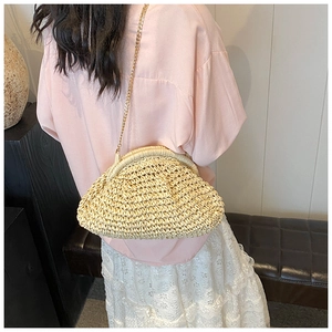 Detail of beige straw woven crossbody bag with gold chain strap on female model
