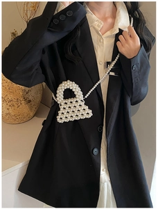 Close-up of handmade white pearl woven crossbody bag on a black blazer outfit