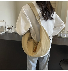 Detailed back view of a beige crescent crossbody bag with adjustable wide strap in a cafe