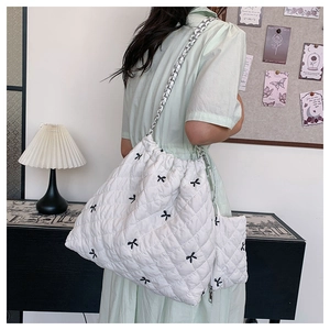 Detail of white quilted tote bag with black bow embroidery and silver chain strap