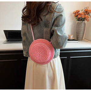 Vista dettagliata di una borsa a tracolla tonda rosa con perle e tracolla sottile