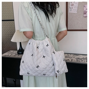 Detail of white quilted tote bag with black bow embroidery and silver chain strap