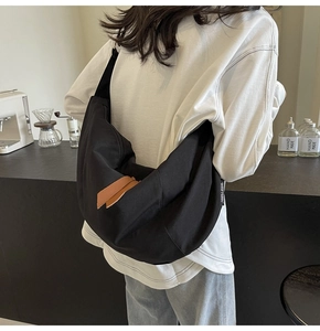 Close-up of black nylon crescent crossbody bag featuring brown leather zipper pull detail