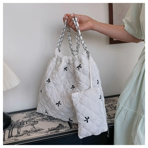 Detail of white quilted polyester tote bag with black bow embroidery and chain strap