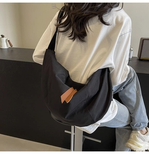 Detail of minimalist black nylon crescent crossbody bag with brown leather zipper puller