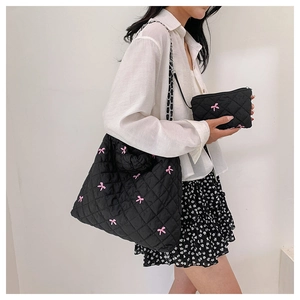 Detailed shot of black quilted polyester tote bag featuring pink bow embroidery and chain strap