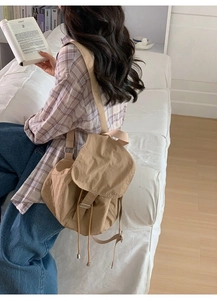 Khaki canvas backpack with drawstring closure shown in a minimalist reading scene