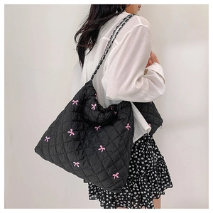 Detail view of black quilted polyester tote bag with pink embroidered bows and chain strap