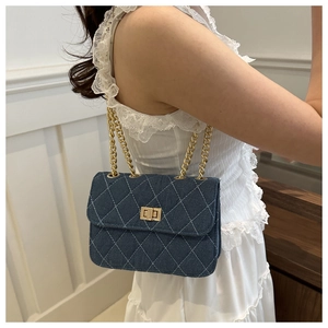 Detail shot of navy denim crossbody bag with white diamond quilting and gold chain strap
