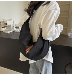 Model wearing a black crescent-shaped fabric crossbody bag in a modern cafe setting