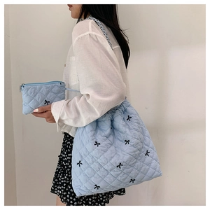 Detailed close-up of light blue quilted tote bag with black bow embroidery and small pouch