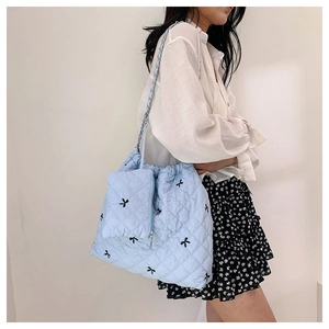 Detail of light blue quilted tote bag with black bow embroidery and silver chain strap