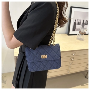 Detail of navy blue quilted denim crossbody bag with bold golden chain strap