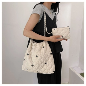 Close-up of beige quilted tote bag set with black bow patterns and silver chain strap