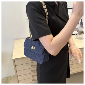 Detail of blue denim crossbody bag with quilted pattern and gold chain strap
