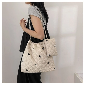 Close-up of quilted beige tote bag featuring black bow embroidery and chain strap detail