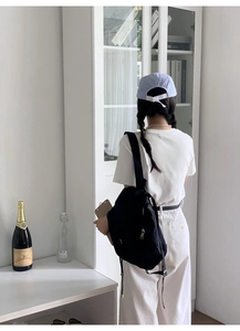 Detailed view of a black nylon backpack on a model standing before a white bookshelf