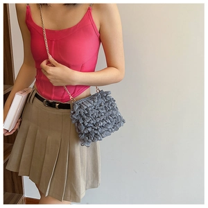 Gray ruffled shoulder bag with gold chain strap shown on model against a minimal wall