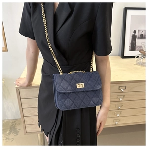 Detail of blue denim quilted crossbody bag with gold chain strap and turn-lock closure