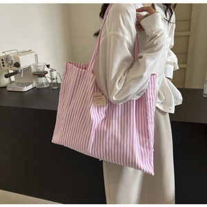 Pink and white striped fabric tote bag with a woven label on a minimalist background