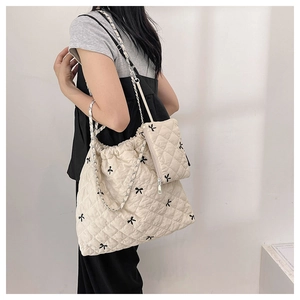 Close-up of beige quilted polyester tote bag with black bow embroidery and chain strap